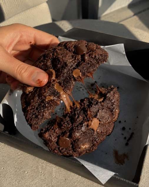 AI render in a candid style: a hand breaking a double chocolate cookie over its box