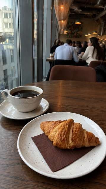 AI render in a candid style: croissant and black coffee by a window