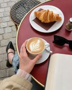 AI render: a hand holding a latte at a pavement table with a croissant