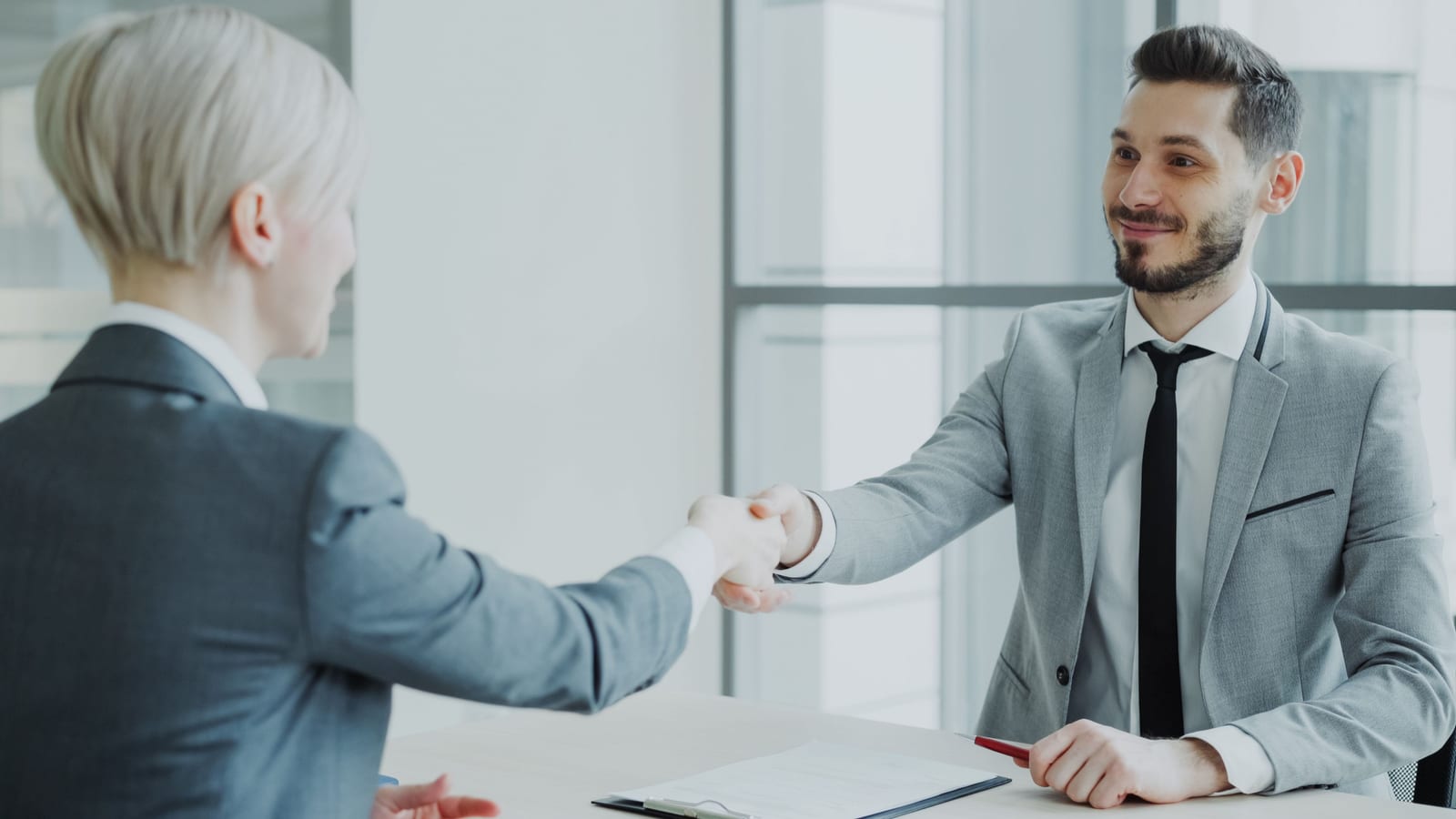 Two colleagues shaking hands across a table at the end of a meeting